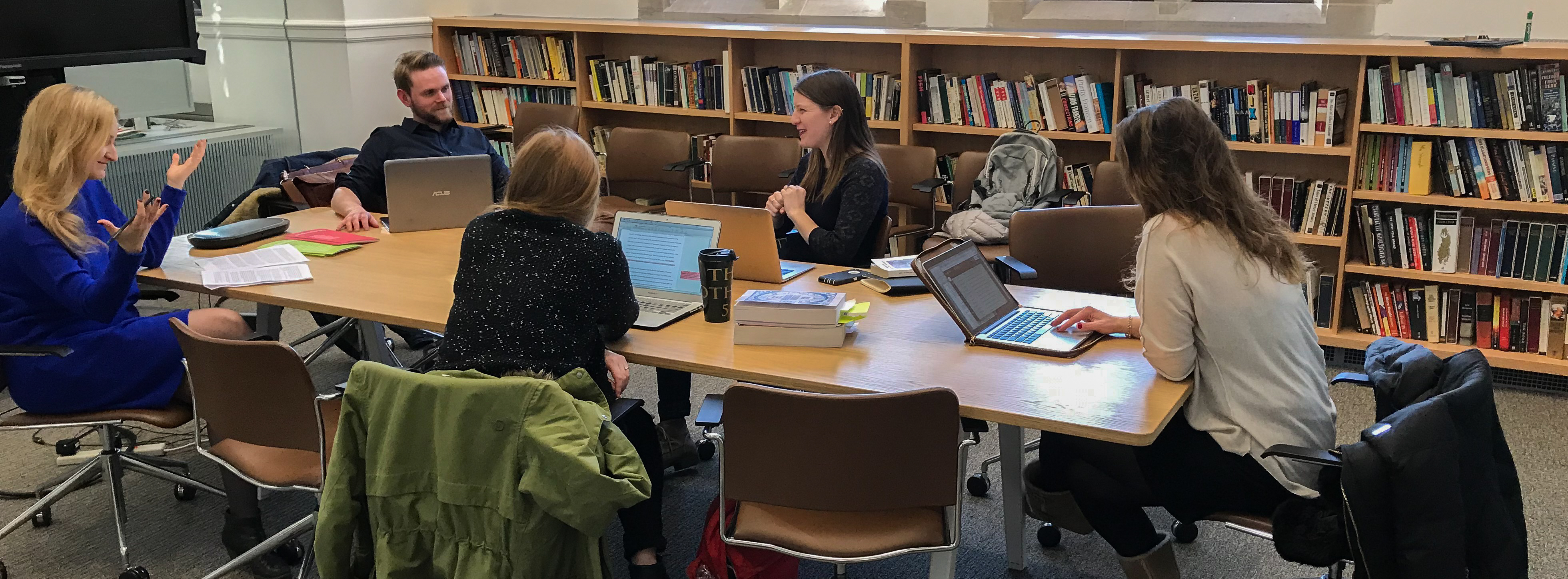 Five graduate students discussing a paper at a small seminar table.