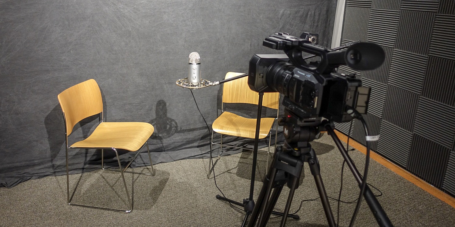 Two chairs flanking a microphone in front of a video camera.
