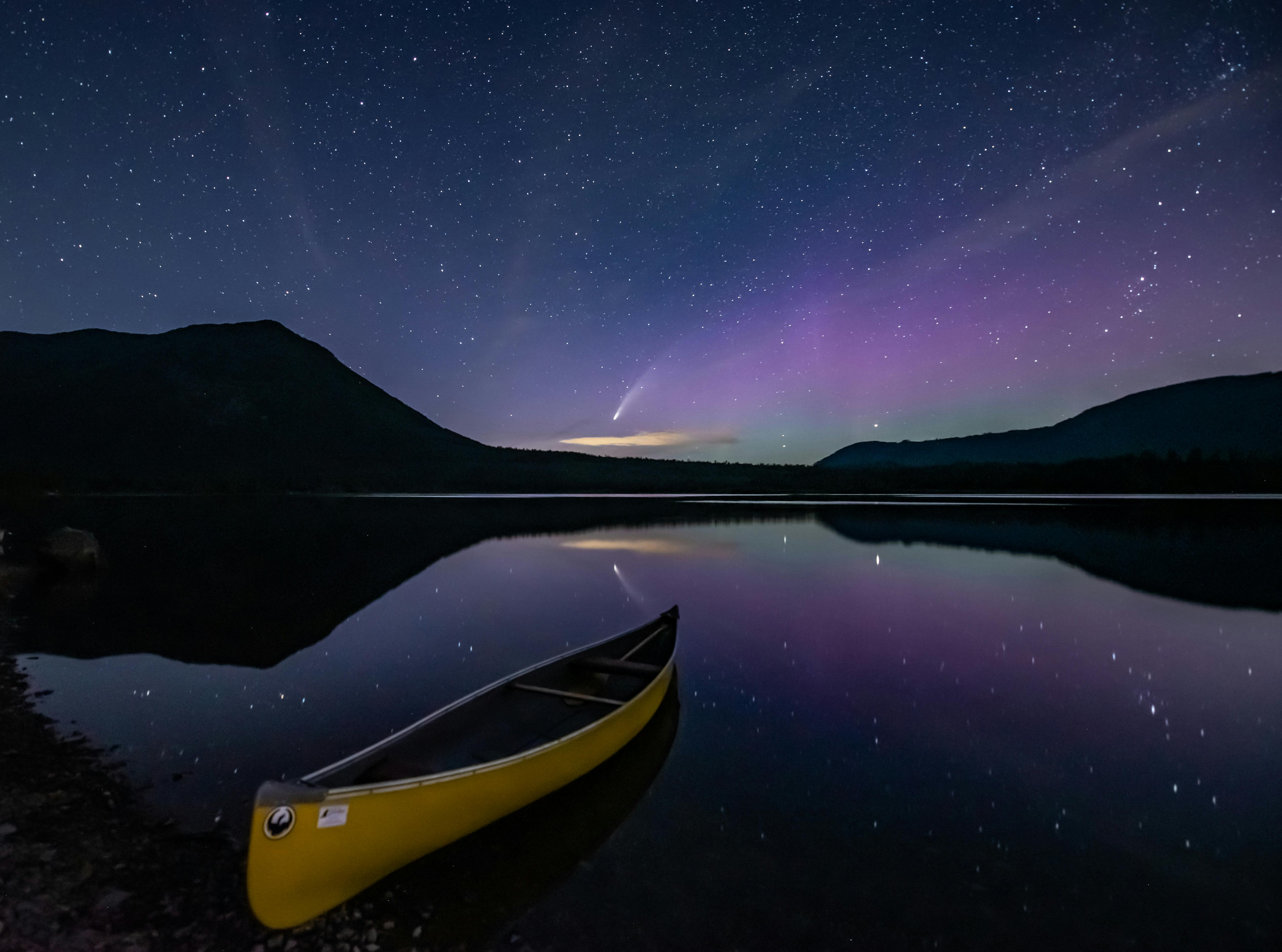 an unoccupied canoe floats still under a night sky full of stars
