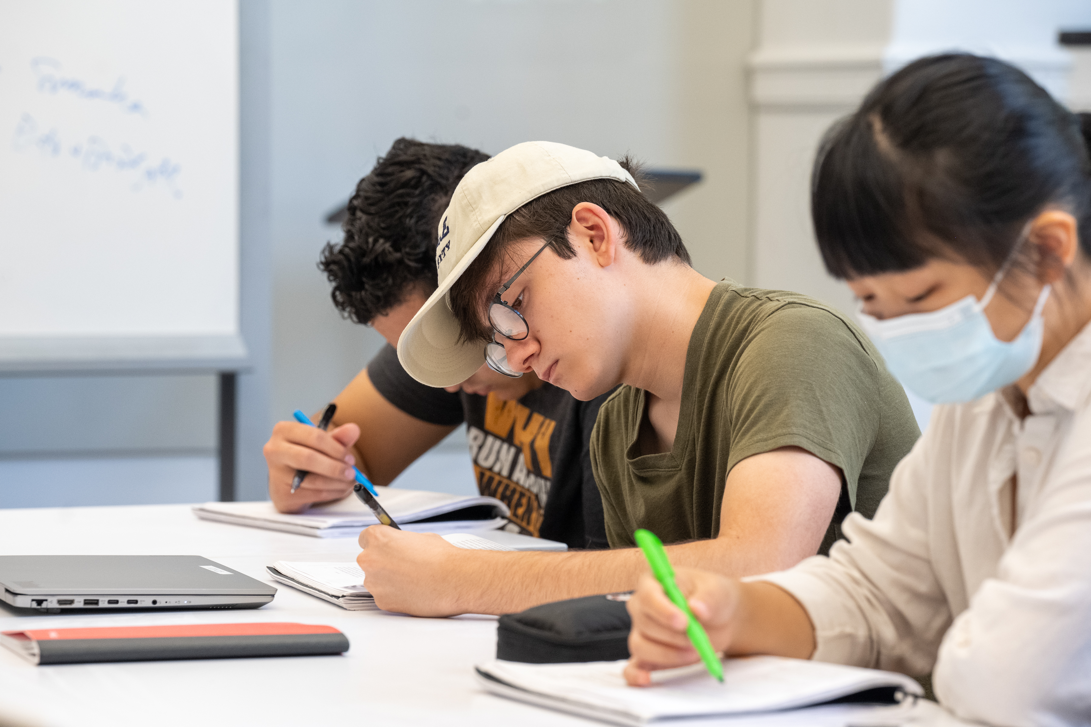 three students at a table writing in notebooks