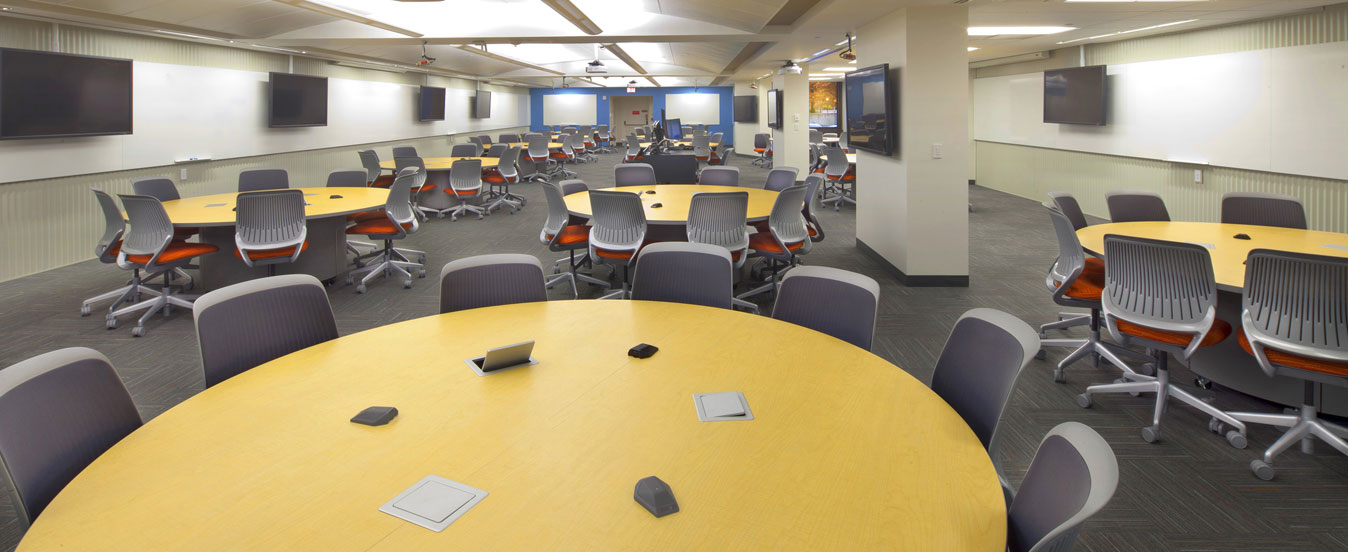 Empty TEAL classroom with multiple empty tables and chairs and various TVs on the walls.