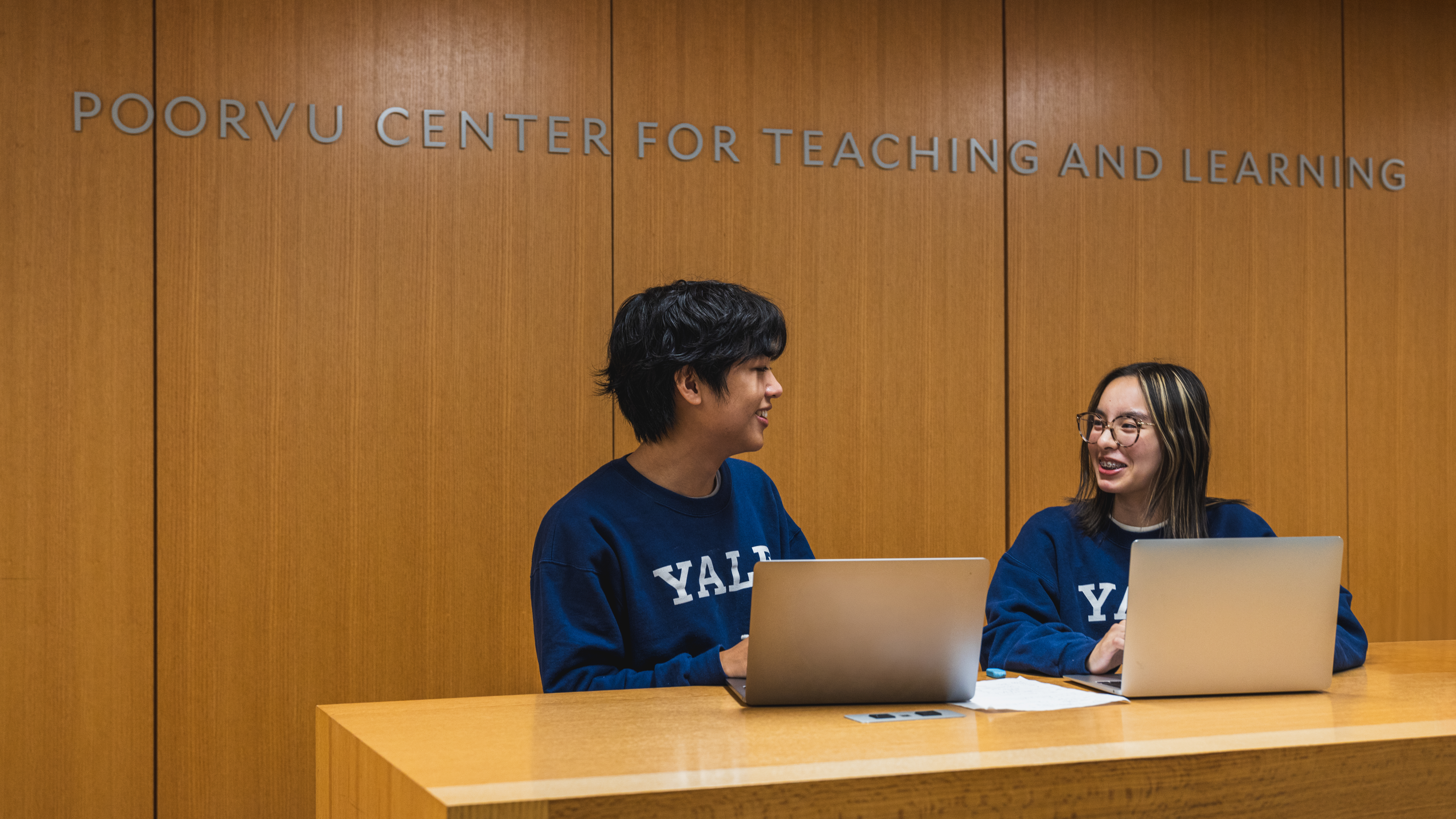 Two students writing together on laptops at the Poorvu Center welcome desk.