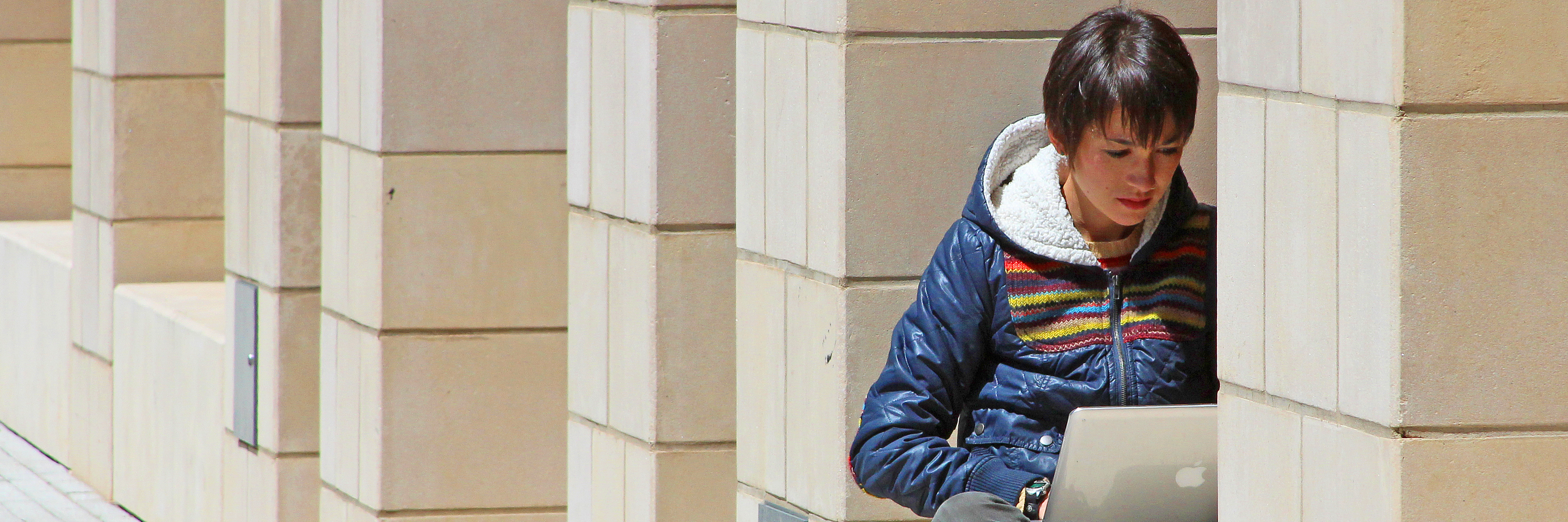 A Yale graduate student typing outdoors on a laptop sitting in the window of a building.