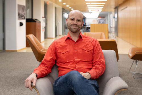 Poorvu Center and Yale Library Create New Leadership Role to Further AI Strategies and Policies Ben Glaser in an orange shirt sitting in the Poorvu Center