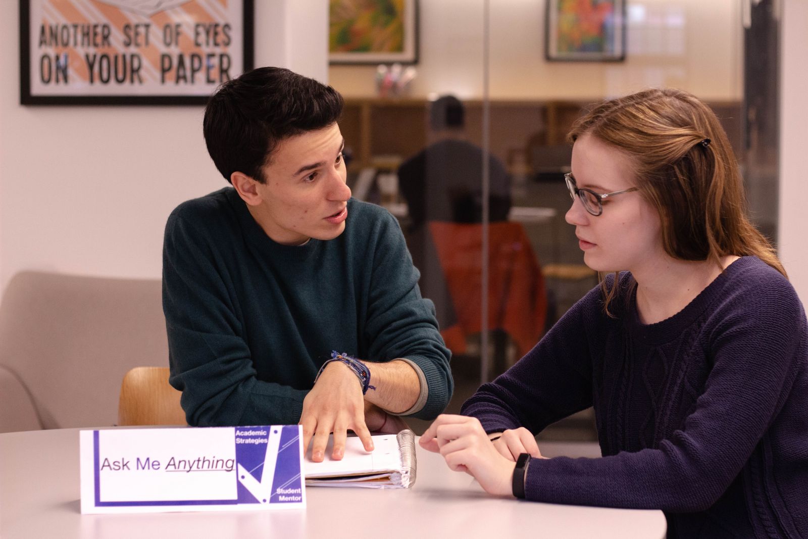 Two students sit at a table in the Poorvu Center. They are talking and concentrating.