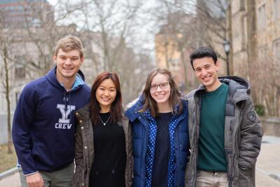 Four ASP Mentors smiling with their arms around each other while they  stand on the Yale Campus in winter.