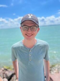 A person wearing glasses and a hat standing on a beachDescription automatically generated