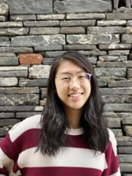 A person smiling in front of a brick wallDescription automatically generated