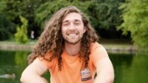 A person with long hair and orange shirtDescription automatically generated