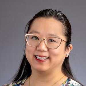 Clare Ankawi in a floral blouse on a grey background.