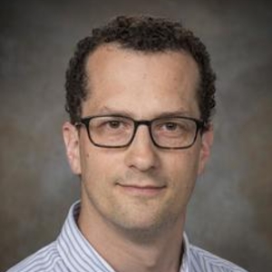 John Harford in a striped blue collard shirt on a grey background