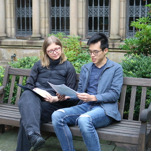 A student and faculty member review a document together sitting on a bench.