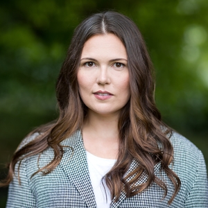 Megan Licskai is a woman with dark brown hair and wearing a gray plaid suit jacket.