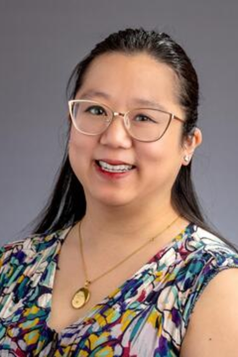 Clare Ankawi in a floral blouse on a grey background.