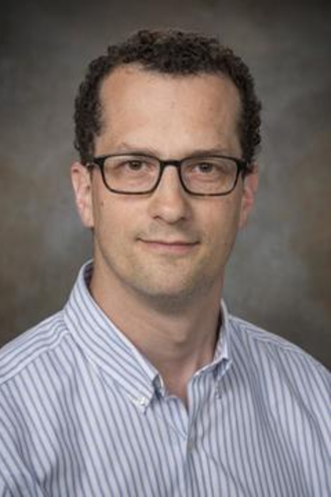 John Harford in a striped blue collard shirt on a grey background