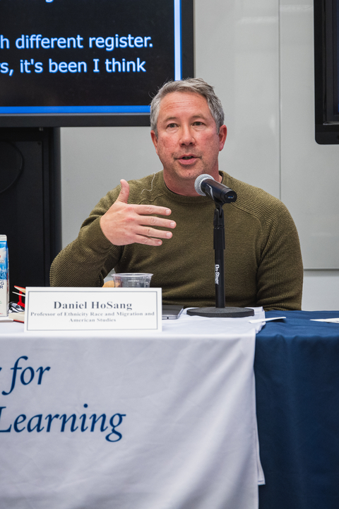 Professor Daniel HoSang, speaks into a microphone while gesturing with his hand during a panel discussion. 