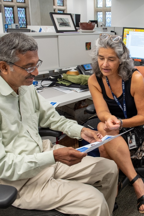 Two Poorvu Center staff members discuss a project while sitting in their office pod.