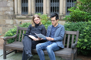 Two graduate students sitting on a bench in a Yale courtyard discussing a paper.
