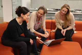 Three students looking at a laptop and discussing a paper together.