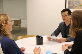 Three grad students exchanging feedback on a paper in a Poorvu Center office.