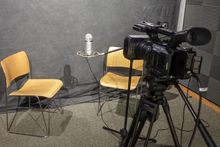 Two chairs flanking a microphone in front of a video camera.