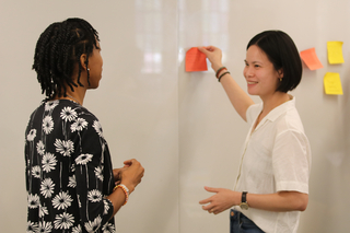 Two Yale graduate students doing a post-it activity at a whiteboard during a Graduate Writing Lab workshop.