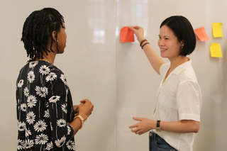 Two Yale graduate students doing a post-it activity at a whiteboard during a Graduate Writing Lab workshop.