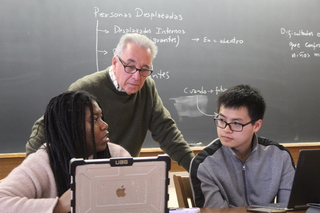 Instructor conferring with two students looking at a laptop