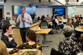 Image of Spring Teaching Forum 2023 with speaker Derek Bruff speaking and participants sitting at round tables
