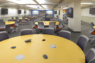 Empty TEAL classroom with multiple empty tables and chairs and various TVs on the walls.
