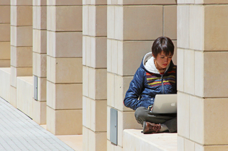 A student writing on a laptop while sitting in a window ledge on a sunny day.