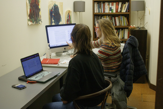A woman sits at a desk and points at her computer while a student at her side looks on.