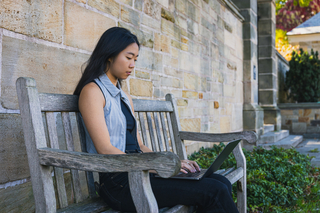 Female student sits on a bench typing on her laptop
