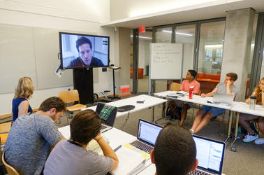 Heather Klemann and several students watch a television screen to interview an expert via ZOOM