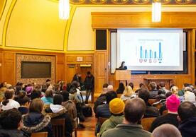 A view of Linsly-Chittenden Hall Room 102 with students and Yale community members seated facing a screen with a PowerPoint slide and a person standing at the podium