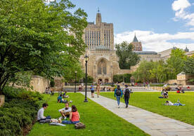 Students sit in groups on the grassy courtyard of Yale's Cross Campus, with Sterling Memorial Library in the background