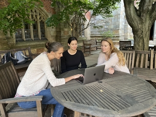 Three students discussing a paper at a table in a Yale courtyard.