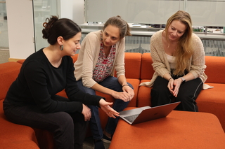 Three students looking at a laptop and discussing a paper together.