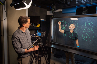 Instructor being filmed while working on a whiteboard