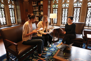 Three students exchanging feedback on a paper in a couch in the library.