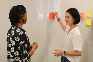 Two Yale graduate students doing a post-it activity at a whiteboard during a Graduate Writing Lab workshop.