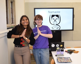 An instructor and an Academic Strategies Mentor hold their palms together; a screen behind them reads, "Namaste."