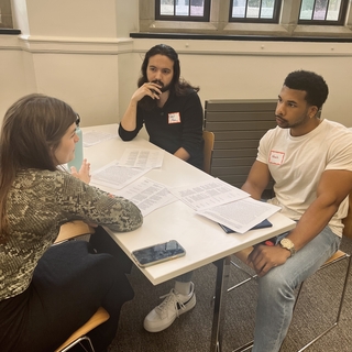 A group of three Writing Partners sit at a table discussing a piece of student writing.