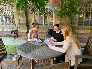 Three Yale Graduate students reading and discussing paper drafts in a Sterling Library courtyard