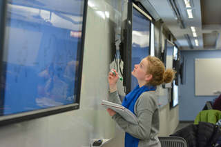Student looking a molecular structure on a screen with a pen and notebook in hand.