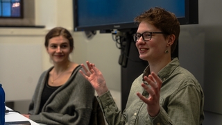 A Writing Partner sits at a table leading a discussion while another Writing Partner looks on.
