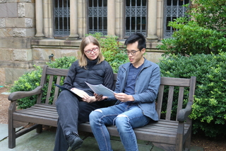 A student and faculty member review a document together sitting on a bench.