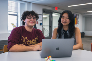 Two Writing Partners sit in front of a laptop at a table on the Poorvu Mezzanine.