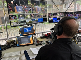 A man sits in a control room looking at monitors during a Yale commencement ceremony