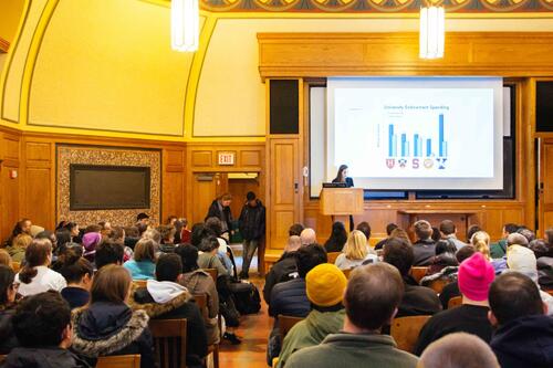 A view of Linsly-Chittenden Hall Room 102 with students and Yale community members seated facing a screen with a PowerPoint slide and a person standing at the podium